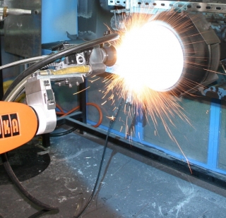 An orange angle grinder sparks as it grinds a metal piece clamped to a blue workbench.