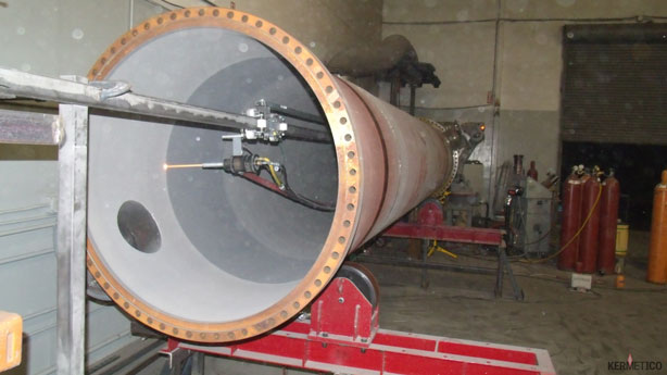 A large cylindrical metal tube with a flanged end mounted on a test stand in a workshop.