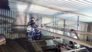 Person wearing a helmet sits on a blue motorcycle inside a metal shed.