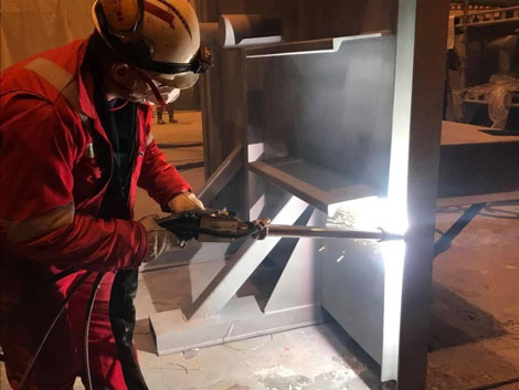 Welder in a red protective suit and helmet welding a metal frame.