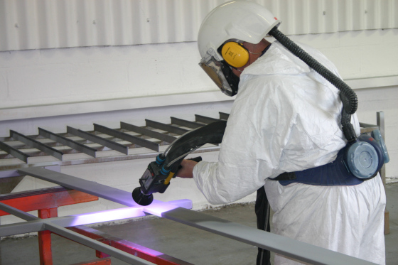 A worker in a white protective suit and helmet plasma-cutting a metal frame in a workshop.