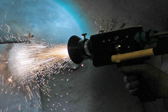 A gloved hand operating a handheld angle grinder that emits bright sparks while grinding metal.