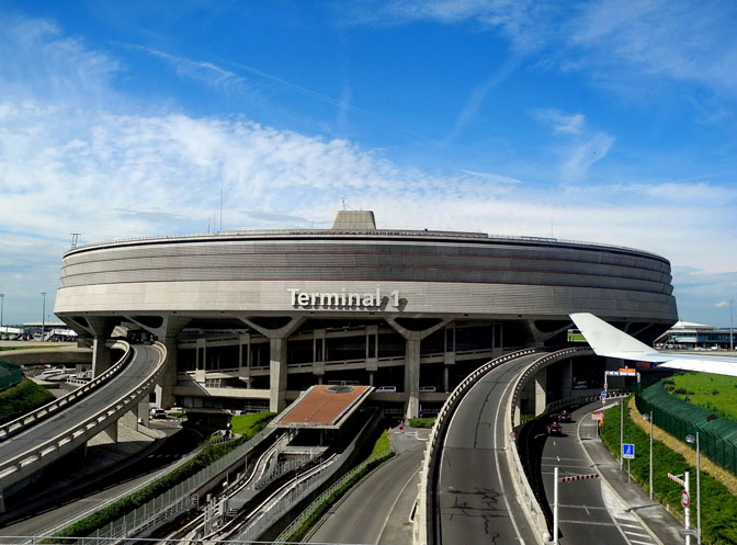 A circular, modern transportation hub with curved elevated roads in front under a blue sky.