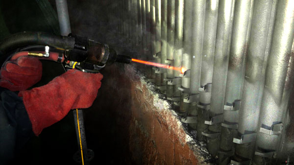 Worker in red gloves using a power tool on a rock wall inside a tunnel with metal support beams.