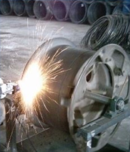 Large metal drum mounted on a frame with a cutting torch emitting bright sparks in a workshop.