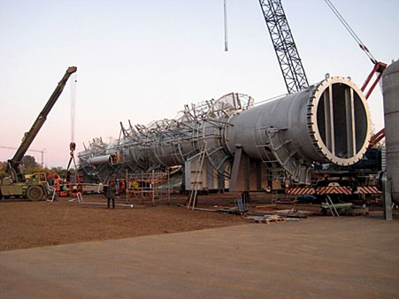 Massive hollow metal pipe section being assembled on a construction site with cranes and workers.