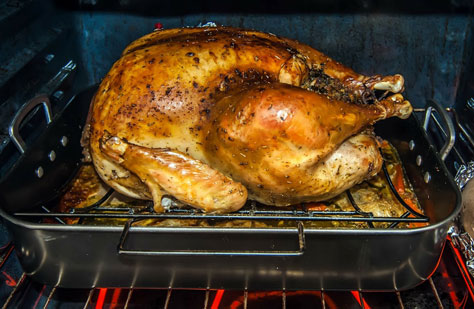 A golden-brown whole turkey sits in a metal roasting pan on a rack inside an oven.