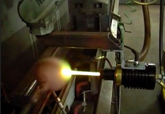 A bright yellow torch flame heats a metal rod inside a laboratory machine.