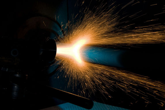 Welding arc with bright orange sparks flying from a metal seam against a dark background.