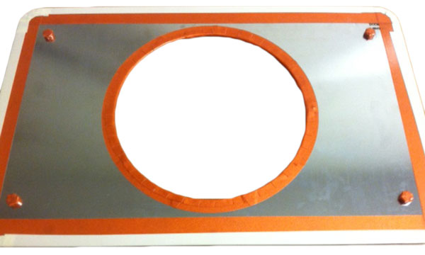 Rectangular metallic plate with an orange border and a large central circular hole, secured by four screws at the corners.