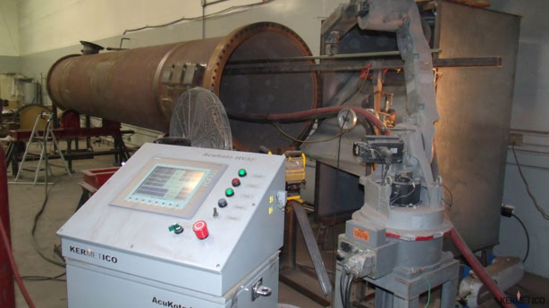 A large horizontal industrial rotary drum machine with a control panel in the foreground inside a workshop.