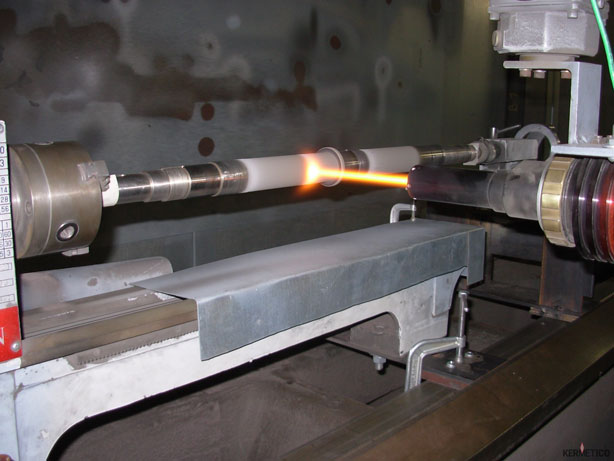 A long cylindrical metal rod is heated by a flame inside an industrial machine, with clamps holding it in place.