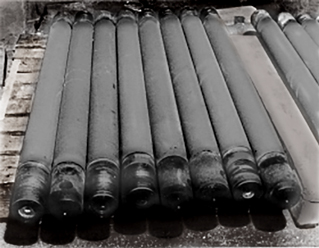 Several dark metal pipes lined up on a concrete surface beside a brick wall.