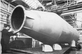 A large rocket engine nozzle mounted on a testing stand in an industrial facility.