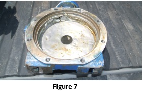 Rusty circular flange with a central bore and multiple bolt holes, mounted on a blue machine frame.