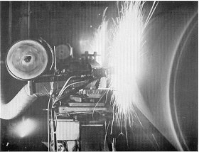 Black-and-white industrial welding scene with a bright arc spark and heavy machinery.