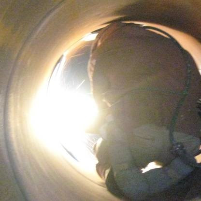 Astronaut in a spacesuit inside a curved metal tunnel with bright light at the end.