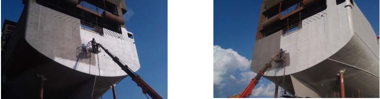 Bow of a large ship resting on red supports in a dry dock against a blue sky.