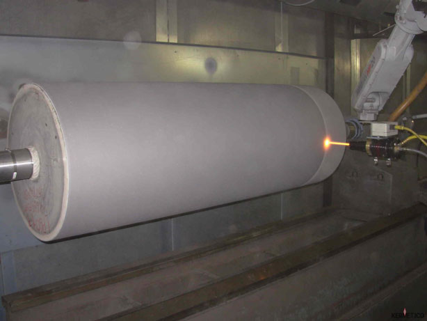 A large white cylindrical roller is being machined on a horizontal lathe, with sparks at the cutting point.