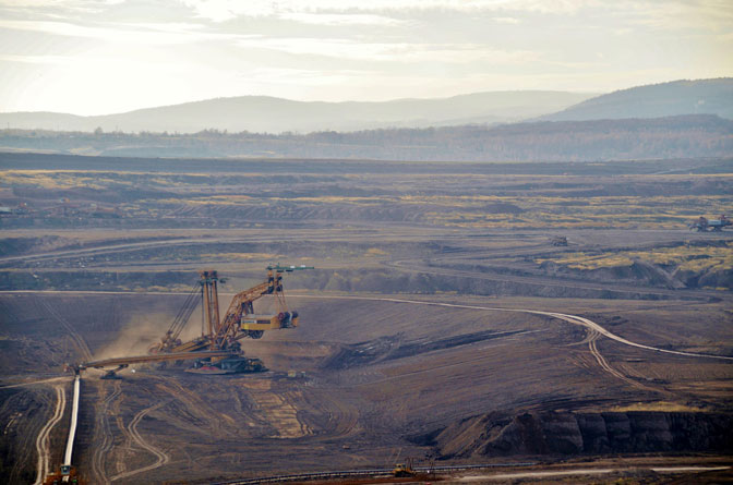 Aerial view of an open-pit mine with heavy machinery and winding roads across a barren landscape.