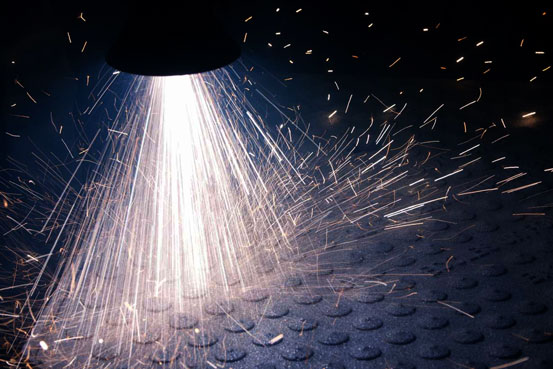 Bright sparks and a glowing jet from a metal grinding operation above a textured metal surface.