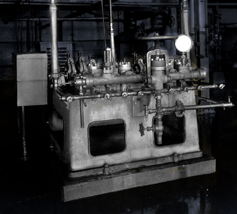 Industrial pump with pipes, valves, and gauges mounted on a concrete base.