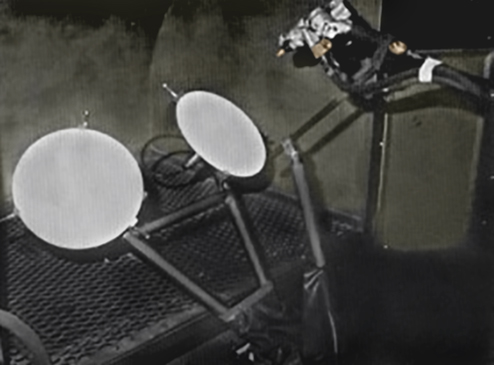 Two white circular satellite dishes attached to a metal frame above a grated surface in a dark setting.