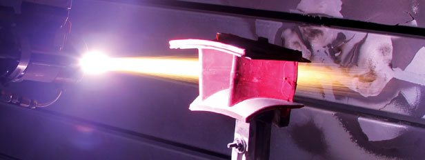 Close-up of a red bench vise gripping metal with a bright welding arc lighting the scene.