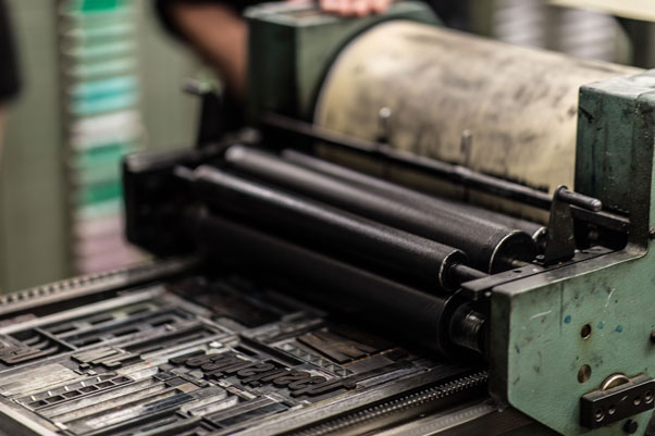 Industrial printing press with large black rollers feeding printed sheets through a green machine.