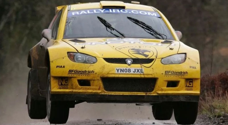 Yellow rally car racing on a dirt road with its front wheels off the ground.