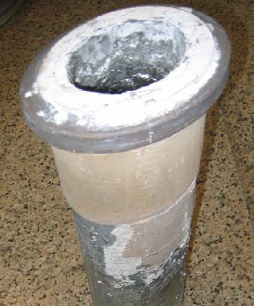 A vertical concrete pipe with a circular metal rim at the top and a hollow opening, set on a speckled floor.