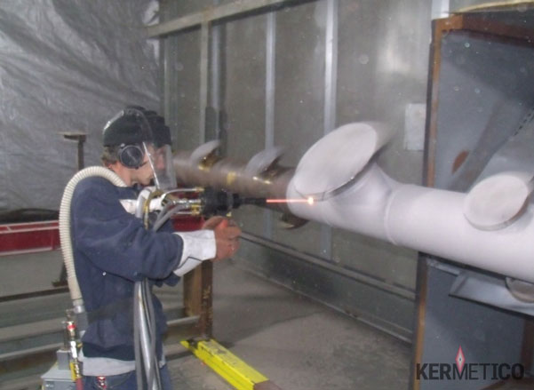 A worker in protective gear arc-welds a metal pipe in an industrial workshop.