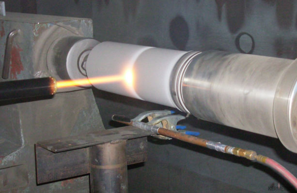 A propane torch heats the end of a white cylindrical tube clamped in a metal vise.