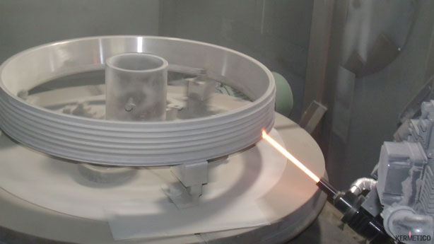 Robotic welding torch glows orange as it welds the edge of a large circular workpiece on a rotary machine.