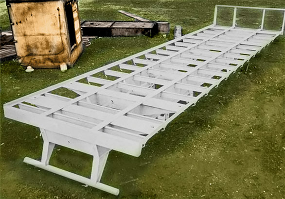 A long white metal frame with evenly spaced rectangular openings sits on a grassy field.
