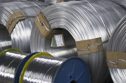 Stacks of large, shiny metal coils secured with cardboard spacers in a warehouse.