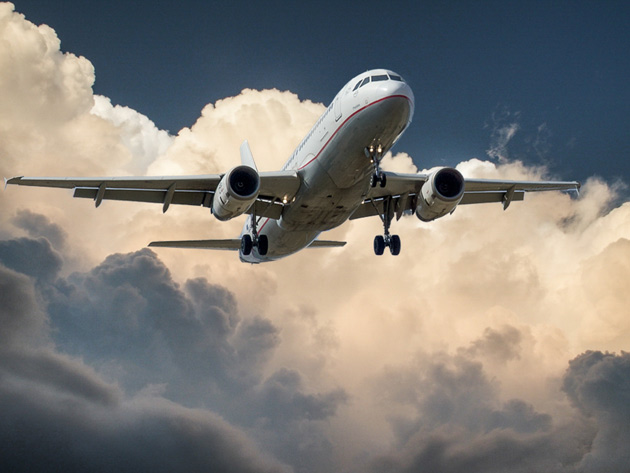 A commercial airliner flying toward the camera with landing gear extended against a cloudy sky.