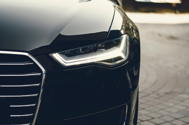 Close-up of a black car's front end with a sleek LED headlight and chrome grille.