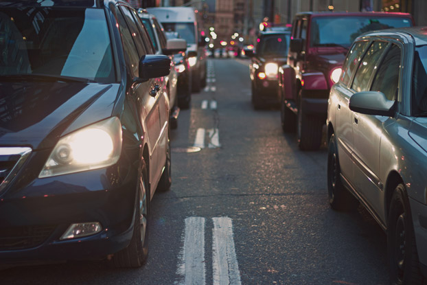 A busy city street at dusk with cars in heavy traffic and their headlights on.