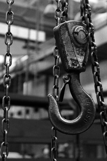 Close-up of a heavy metal hook hanging from chains in an industrial workshop.