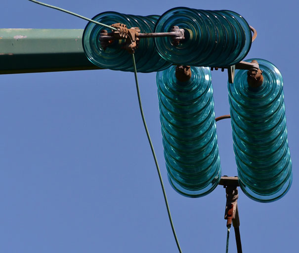 Close-up of green spiral insulators on a high-voltage power line against a blue sky.