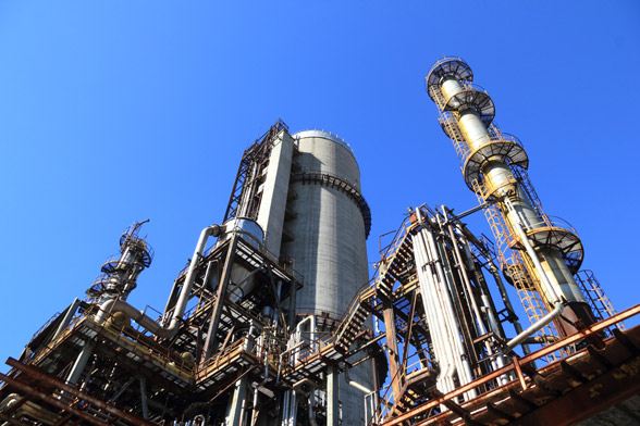 Industrial refinery with tall distillation columns and extensive piping against a clear blue sky.