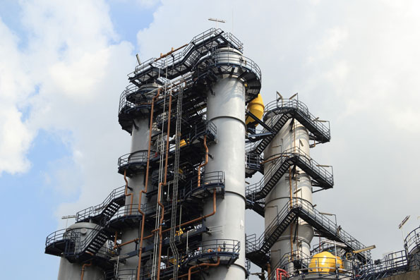 A large industrial refinery complex with tall vertical towers, external metal staircases, and extensive piping.
