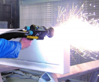 Person in a blue sleeve uses a handheld angle grinder to cut metal, producing sparks in a workshop.