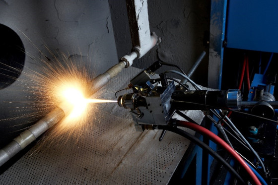A welding torch sparks as it welds a metal plate on a fixture.