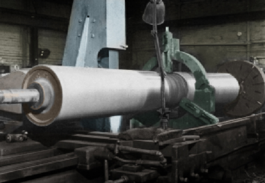 A large white cylindrical roller mounted on a green industrial machine in a factory workshop.