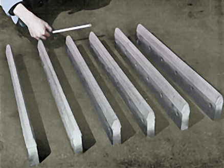 A hand holding a tool beside a row of long rectangular concrete blocks laid diagonally on a wet surface.