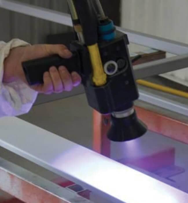 A person holding a black handheld tool that emits a purple light onto a metal surface.