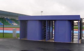 Blue curved shelter with an open central entrance showing stairs, on a dark paved area.