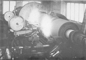 Black-and-white photograph of an old industrial engine with a large flywheel, gauges, and piping.
